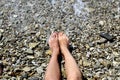 Women`s feet lie on a pebble beach washed by sea water. Royalty Free Stock Photo