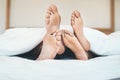 Feet of an in love couple lying in bed, relaxing and bonding together at home. Closeup of a barefoot boyfriend and Royalty Free Stock Photo