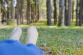 feet lying resting on grass in pine tree forest. leg wearing jeans relaxing in park Royalty Free Stock Photo