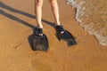 Feet of a man in black flippers on the beach