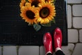 feet in red shoes beside sunflower bouquet on a black welcome mat