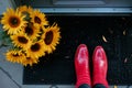 feet in red shoes beside sunflower bouquet on a black welcome mat