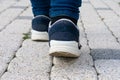 Feet in running shoes are walking forward on stony road.