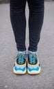 Feet shod in sneakers multi-colored yellow, white, black and blue are on the asphalt road.