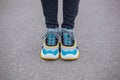 Feet shod in sneakers multi-colored yellow, white, black and blue are on the asphalt road.