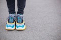 Feet shod in sneakers multi-colored yellow, white, black and blue are on the asphalt road.