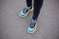 Feet shod in sneakers multi-colored yellow, white, black and blue are on the asphalt road.