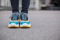 Feet shod in sneakers multi-colored yellow, white, black and blue are on the asphalt road.