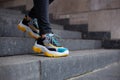 Feet shod in sneakers multi-colored yellow, white, black and blue down the stairs