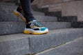 Feet shod in sneakers multi-colored yellow, white, black and blue down the stairs