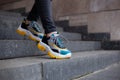 Feet shod in sneakers multi-colored yellow, white, black and blue down the stairs