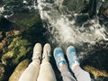 Feet in sneakers on the rocks, selfie over a fast river in the background. Top view of female and male legs over bubbling water. Royalty Free Stock Photo