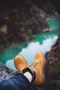 Feet of traveler in boots over chasm with river canyon