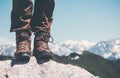 Feet trekking boots on rocky cliff with mountains landscape