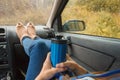 Feet in warm cute socks on car dashboard. Travel, road trip and autumn fall concept. Focus on thermos bottle cup with hot drink