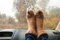 Woman legs in warm cute socks on car dashboard. Drinking warm tee on the way. Fall trip. Rain drops on windshield. Freedom travel Royalty Free Stock Photo