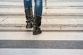 Feet of a woman with boots walking on the white strips of a pedestrian zebra crossing, or crosswalk, to pass a street and road use