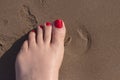 Feet of woman with nails painted red on the sand of the sea Royalty Free Stock Photo