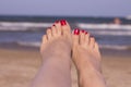 Feet of woman with nails painted red on the sand of the sea Royalty Free Stock Photo