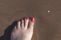 Feet of woman with nails painted red on the sand of the sea Royalty Free Stock Photo