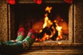 Feet in woollen socks by the fireplace. Woman relaxes by warm