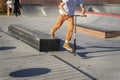 Feet in yellow sneakers and pants of teenager jumping a kick scooter at a skate park. Street culture of young