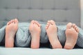 The feet of a young couple on the bed, closeup. Boyfriend and girlfriend lying in bed under blanket. Family bedroom Royalty Free Stock Photo