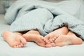 Feet of a young couple lying on the bed at honeymoon. Couple in love. Love lying in bed in hotel. Close up legs under stripes Royalty Free Stock Photo