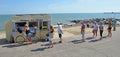 Distanced queue for ice cream on sea front promenade beach and sea in background.