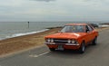 Classic Orange Ford Cortina MK3 Car being driven along seafront promenade beach and sea in background. Royalty Free Stock Photo