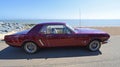 Classic Purple Ford Mustang parked on seafront beach and sea in background.