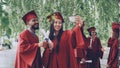 Fellow students are taking selfie with diplomas posing and smiling, girl is holding smartphone, people are wearing gowns