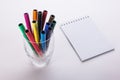 Felt-tip pens in a glass and a notebook on a white background