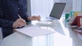 A female accountant is using a laptop computer and calculator to calculate taxes at a glass desk in the office