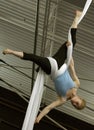 A female acrobat hangs upside down by wrapping aerial silks around her waist and legs.