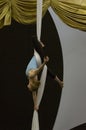 A female acrobat suspends herself upside using aerial silks around her waist and legs.