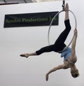 A female acrobat swings upside down from an aerial hoop.