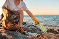 A female activist collects plastic bottles in a garbage bag. Close-up, out of focus. The sea is in the background. Copy Royalty Free Stock Photo