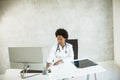 Female African American doctor wearing white coat with stethoscope sitting behind desk in office Royalty Free Stock Photo