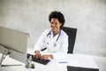 Female African American doctor wearing white coat with stethoscope sitting behind desk in office Royalty Free Stock Photo