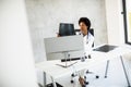 Female African American doctor wearing white coat with stethoscope sitting behind desk in office and looking x-ray image Royalty Free Stock Photo