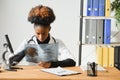 Female African American doctor wearing white coat with stethoscope sitting behind desk in the office and looking x-ray Royalty Free Stock Photo