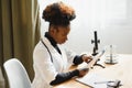 Female African American doctor wearing white coat with stethoscope sitting behind desk in the office and looking x-ray Royalty Free Stock Photo