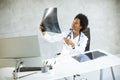 Female African American doctor wearing white coat with stethoscope sitting behind desk in office and looking x-ray image Royalty Free Stock Photo