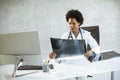 Female African American doctor wearing white coat with stethoscope sitting behind desk in office and looking x-ray image Royalty Free Stock Photo