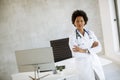 Female African American doctor wearing white coat with stethoscope sitting behind desk in office and looking x-ray image Royalty Free Stock Photo