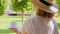 female age 50-55 in a straw hat holds a cup of hot drink and drinks coffee, sitting in the morning on a summer terrace Royalty Free Stock Photo