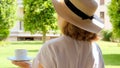 female age 50-55 in a straw hat holds a cup of hot drink and drinks coffee, sitting in the morning on a summer terrace Royalty Free Stock Photo