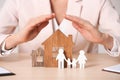 Female agent covering wooden houses and family at table. Home insurance