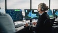 Female Air Traffic Controller with Headset Talk on a Call in Airport Tower. Office Room is Full of